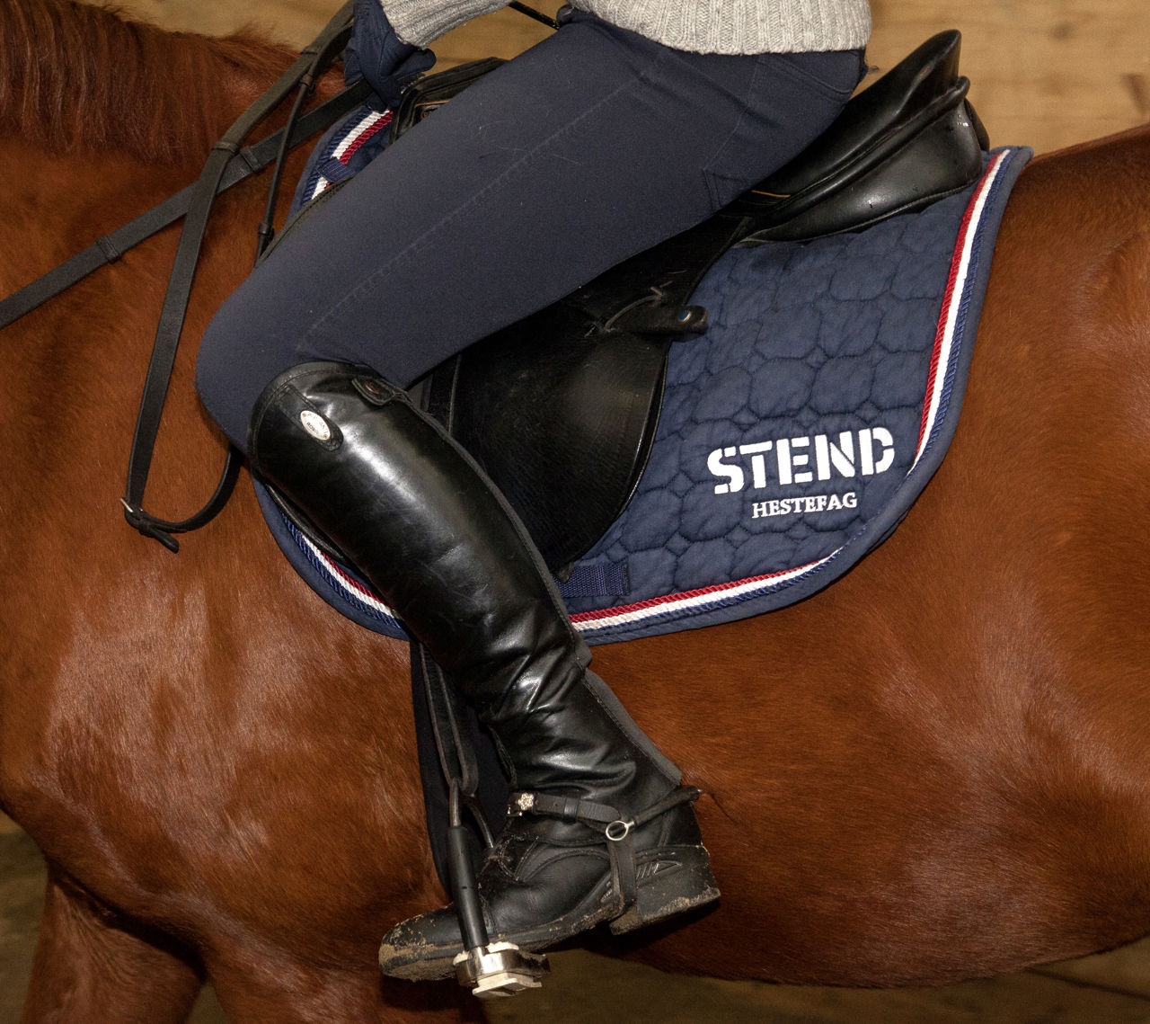 Bildet viser en person fra livet og ned som sitter på en brun hest