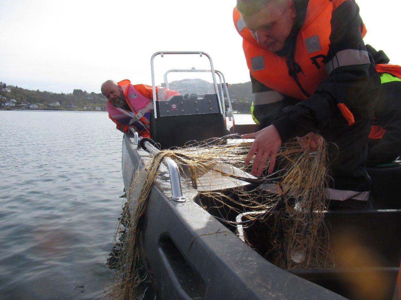 Elev og lærar i båt på fjorden. Elev trekker garn.