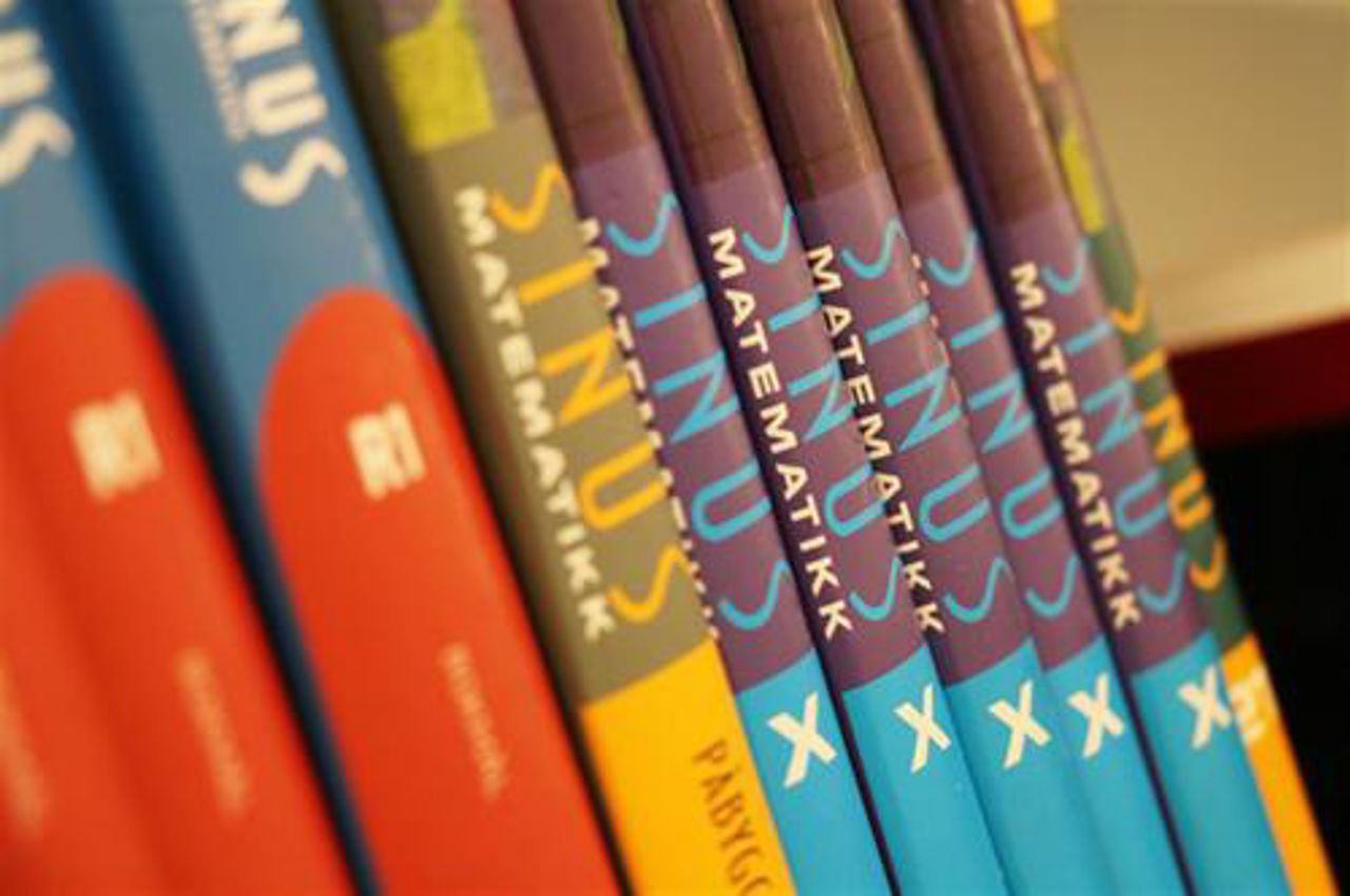 Tre jenter sitter ved et bord. To ser på en PC og en leser i en bok